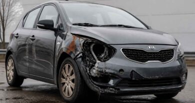 Szara Kia z poważnie uszkodzonym przodem i lewym reflektorem stoi na mokrej nawierzchni